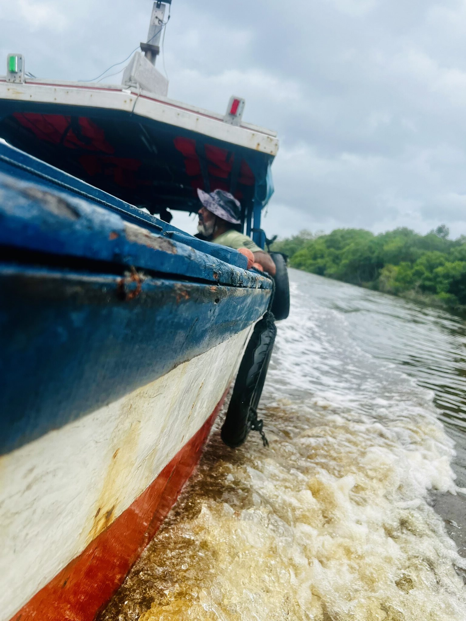 man hangt wat over rand van bootje op de suriname rivier