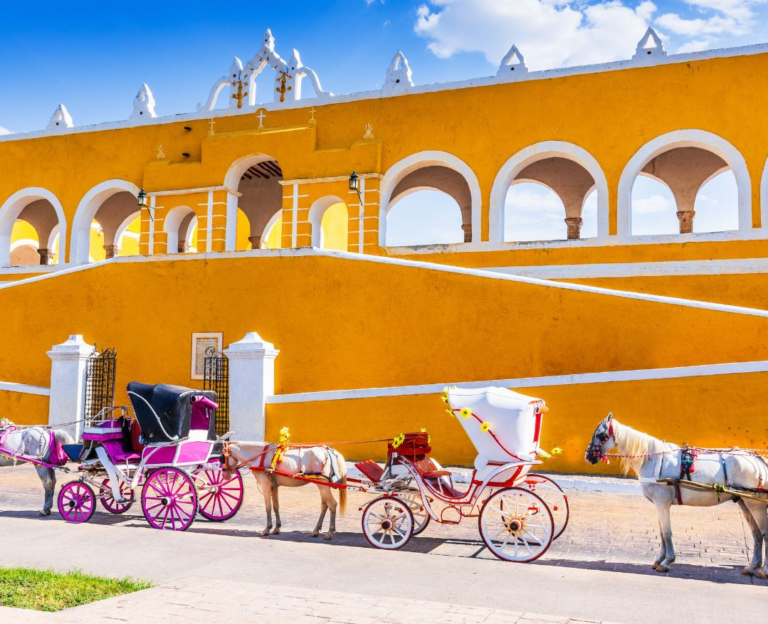 Oranje geel gebouw met op de voorgrond paarden met wagens in Izamal Mexico