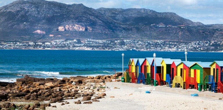 een strand met kleurrijke hutjes langs de kust en Kaapstad aan de andere kant van de baai