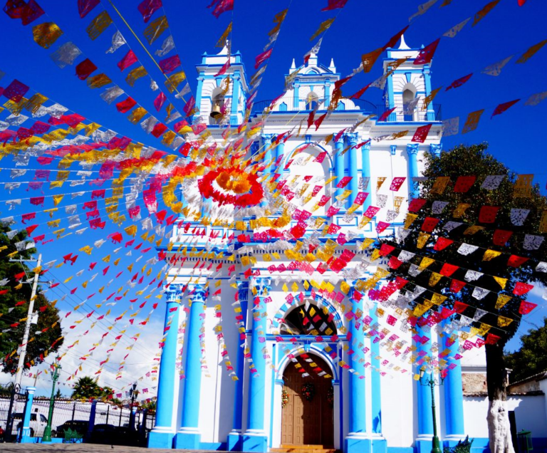 Blauwe witte kerk met op de voorgrond verschillende lijnen met gekleurde vlaggetjes in San Cristobal de las Casas Mexico