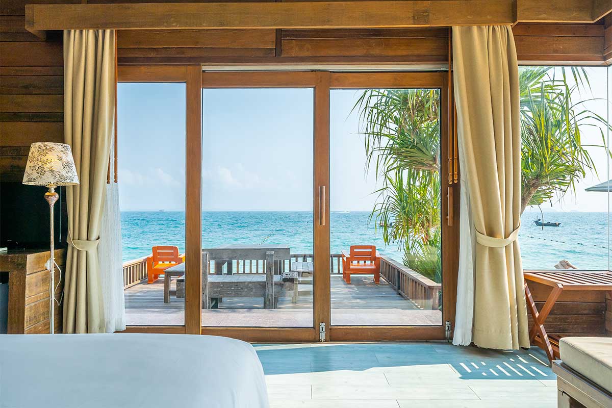 Hotelkamer met glazen deuren die uitzicht geven op helder water en palmbomen in Ko Samed