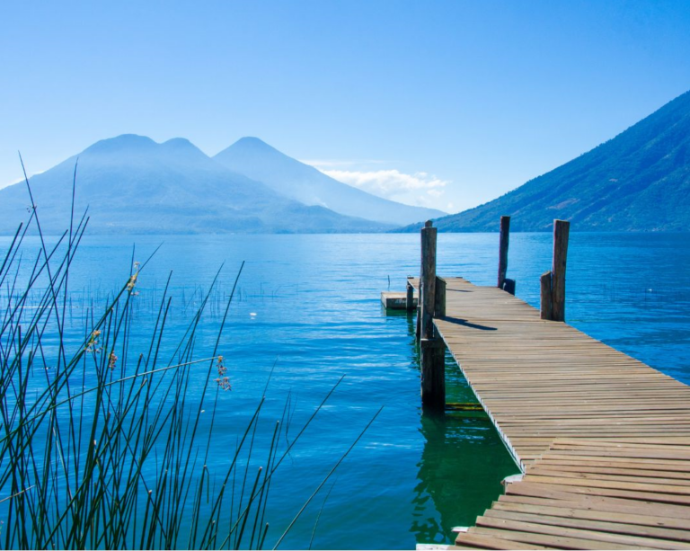 Een steiger lopend het water in van Lake Atitlan met op de achtergrond vulkanen
