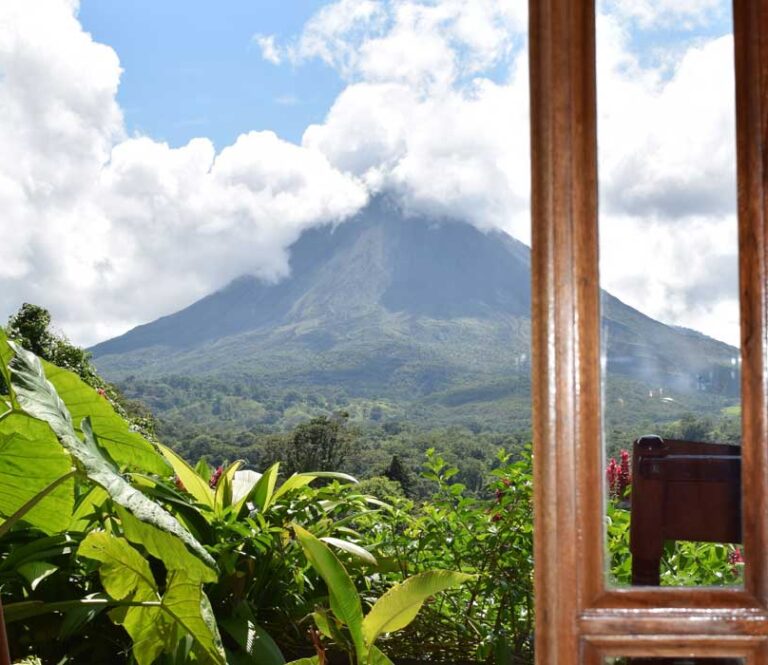 doorkijk vanuit lodge raam op jungle en Arenal vulkaan