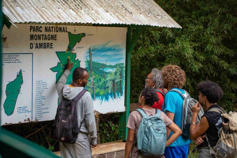 Groepje reizigers bij bord van parc national de montagne d'ambre met gids die wat uitgelegd in Madagaskar
