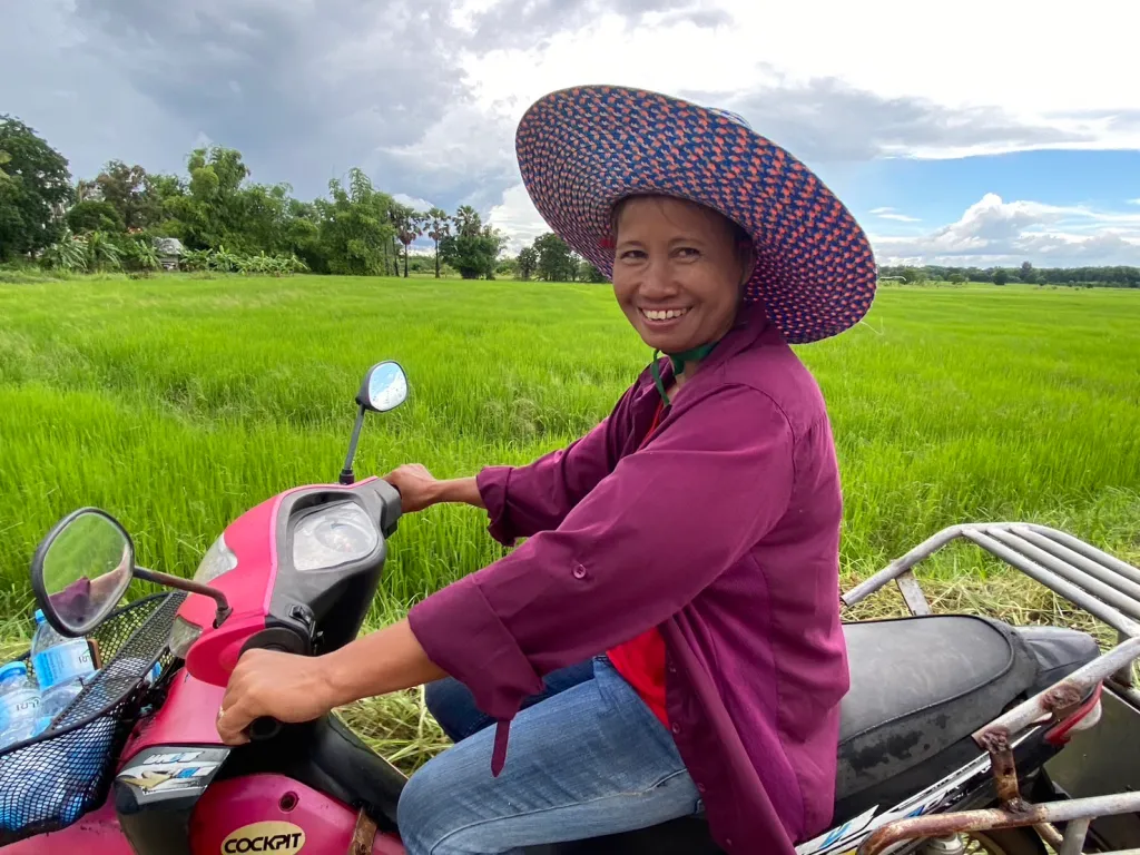 Lokale Thaise vrouw die op haar scooter zit en rijdt door de grasvelden van Thailand