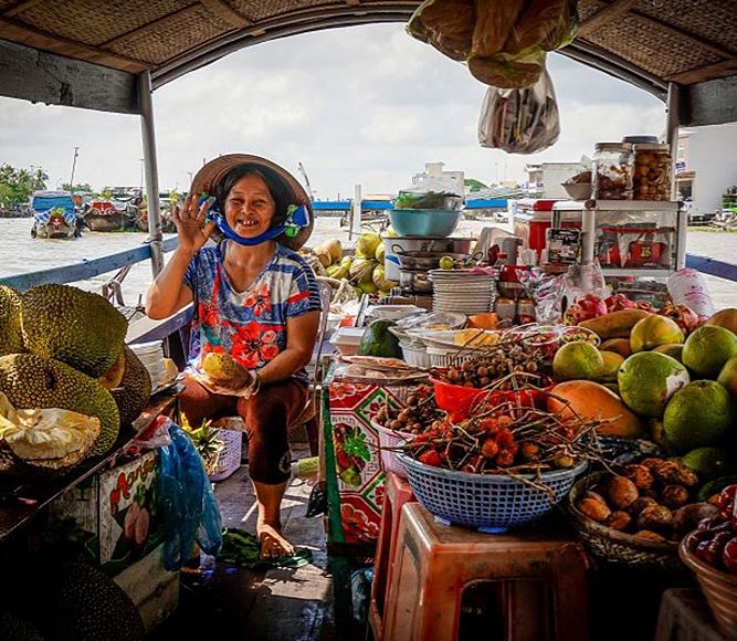 Een Vietnamese vrouw zit op haar boot temidden tafels en krukjes vol met vers fruit