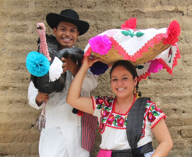 Lokale man en vrouw in Mexico waarbij de vrouw een mand op haar hoofd heeft en de man een kalkoen vasthoudt