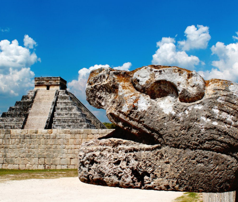 Rots in de vorm van een gezicht met op de achtergrond een Maya ruïne bij Chichen Itza Mexico