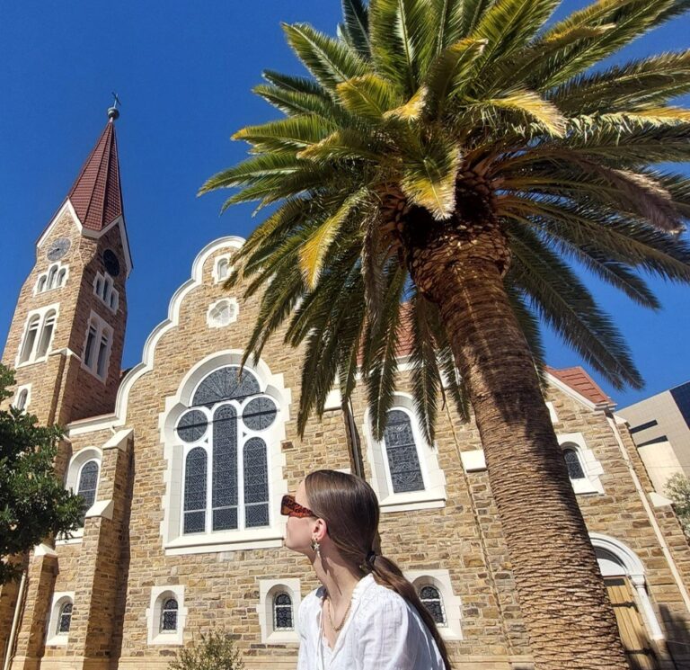 vrouw onder palmboom kijkt naar kerk in windhoek