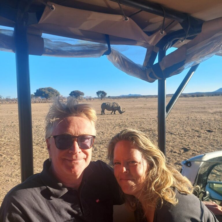 reizigerskoppel in safari jeep poseert met op achtergrond olifanten op de zandvlakte