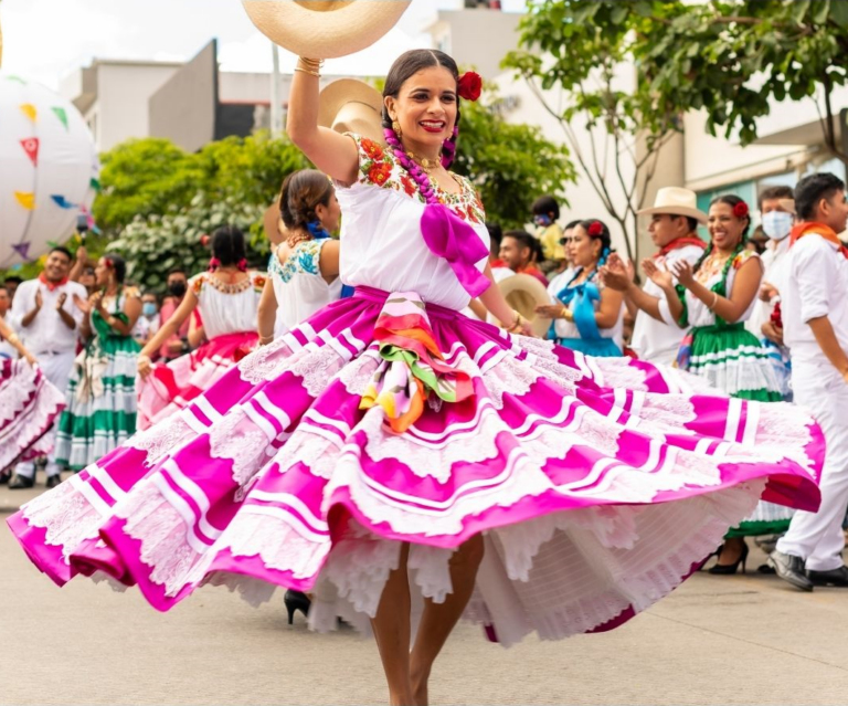 Dansende vrouw in roze witte jurk met hoed in haar hand in Mexico en op de achtergrond meerdere locals