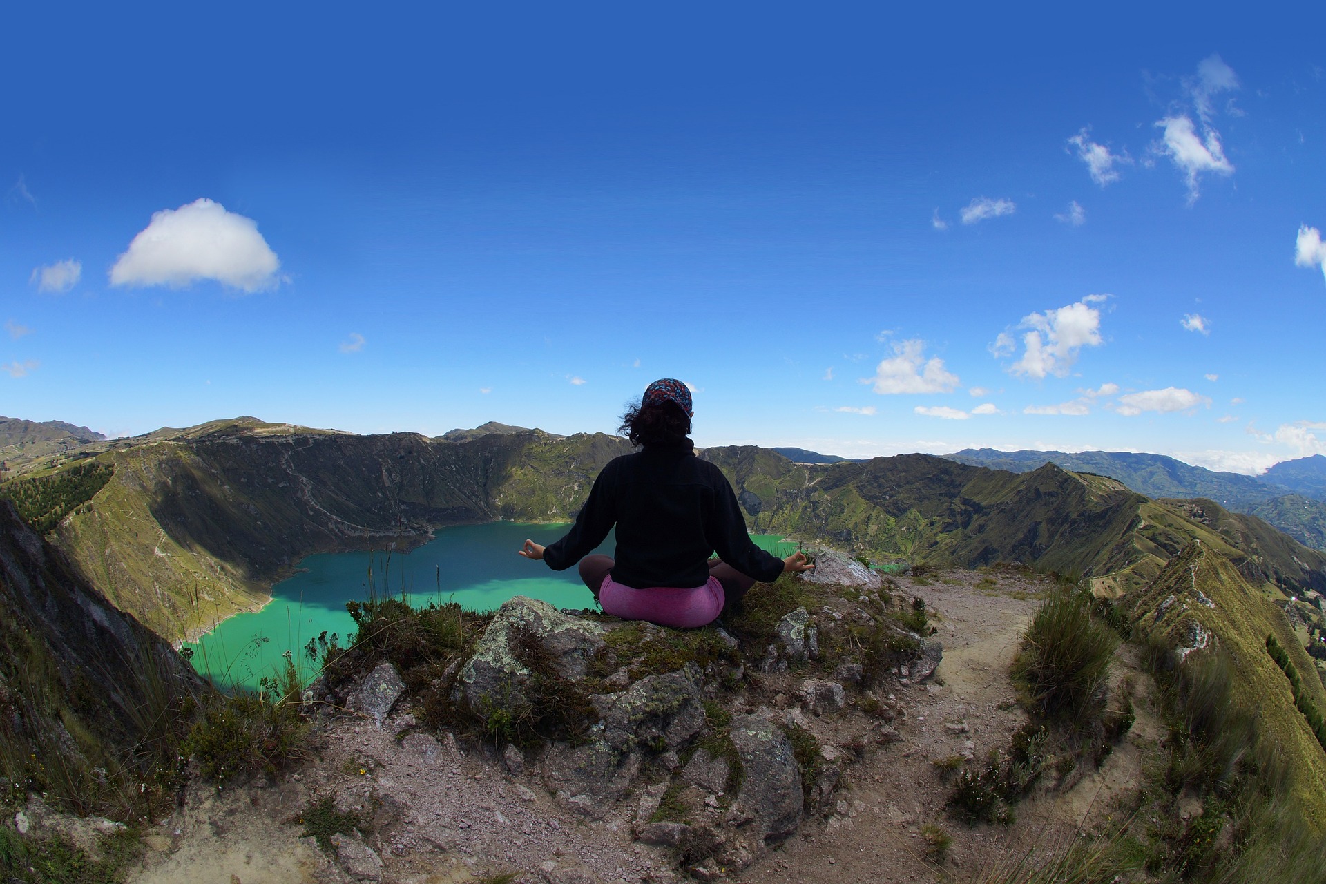 vrouw zit op rots bij vulkaankrater met blauw water in ecuador