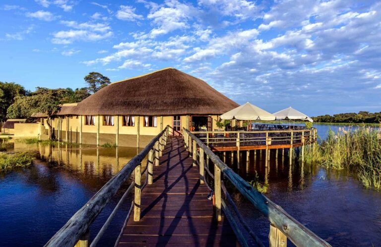 houten brug over rivier naar lodge met rieten dak