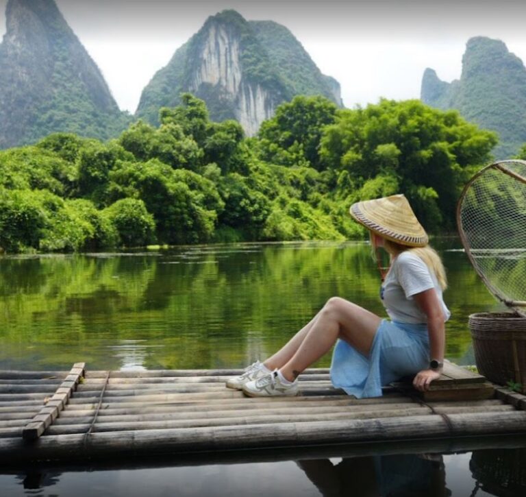 vrouw met puntige aziatische hoed vaart per bamboevlot over Li-rivier China omgeven door karstbergen