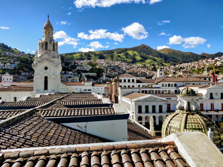 uitzicht over de daken van Quito, erbovenuit steekt een toren en op de achtergrond een groen en heuvelachtig landschap