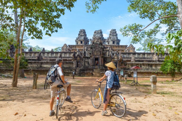 twee mensen op de fiets staan voor een groot historisch tempelcomplex in Cambodja