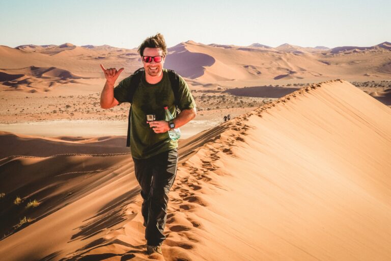man loopt enthousiast over rode duintop van sossusvlei