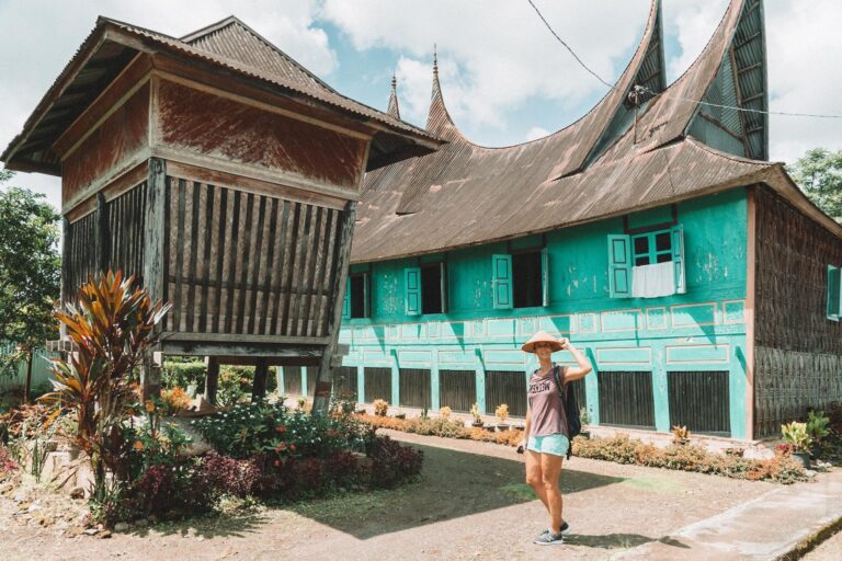 Een reizigster poseert met rieten hoe voor een Rumah Gadang, een traditioneel huis van de Minangkabau in West-Sumatra