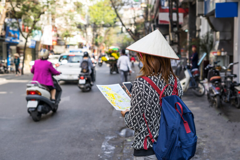 een toerist staat op straat en kijkt op een kaart, ze heeft een traditionele Vietnamese hoed op