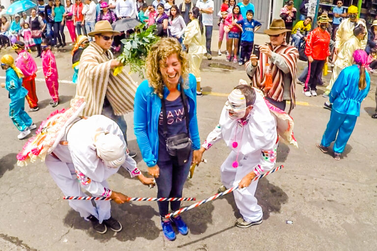 een toerist wordt meegenomen middenin een traditionele viering, mensen in Ecuadoraanse feestkleding met kleurrijke stokken