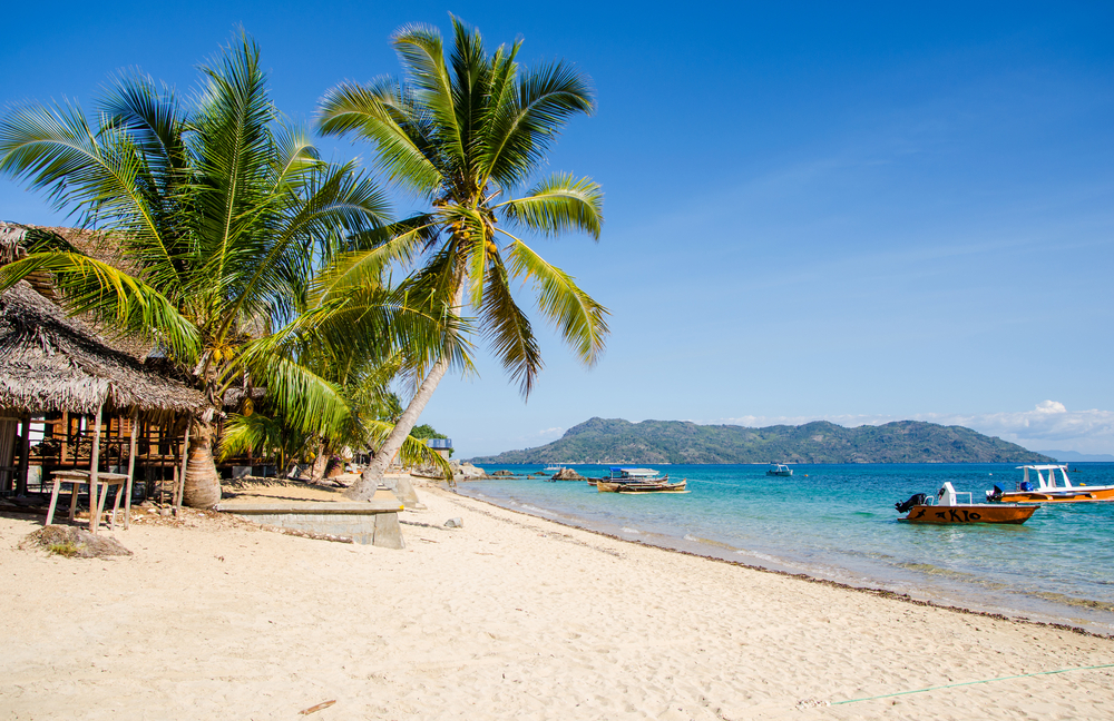wit strand met palmbomen en turquoise zee met bootjes op madagaskar