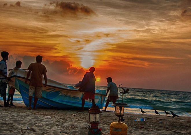 vissers halen blauwe houten boot uit zee bij zonsondergang sri lanka