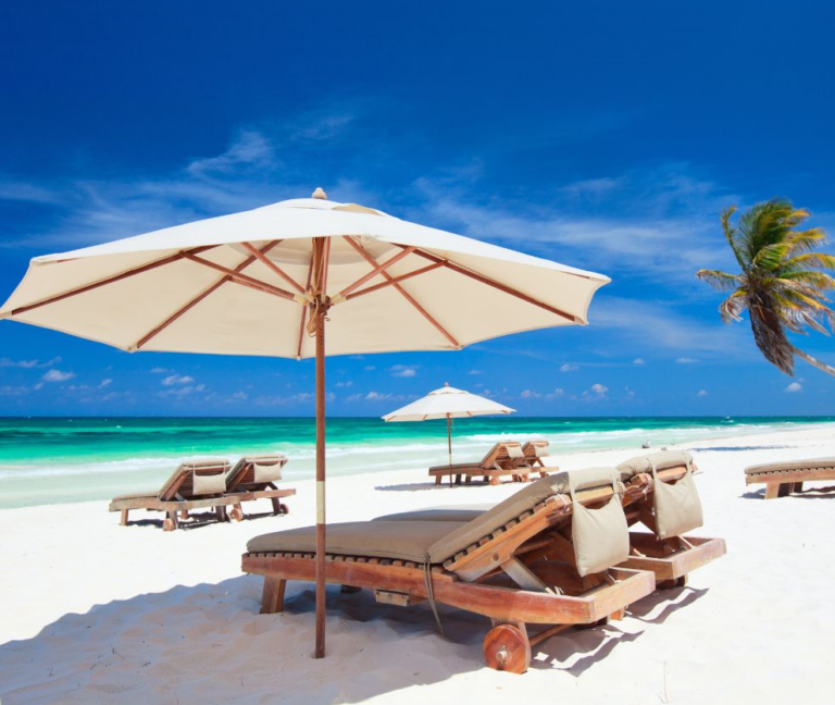 Strandbedjes met parasol kijkend op de azuurblauwe zee van Mexico