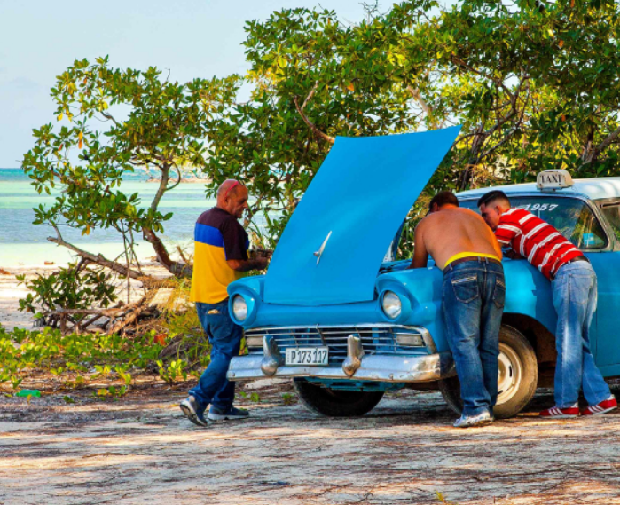 locals kijken bij blauwe auto onder de motorkap op cuba