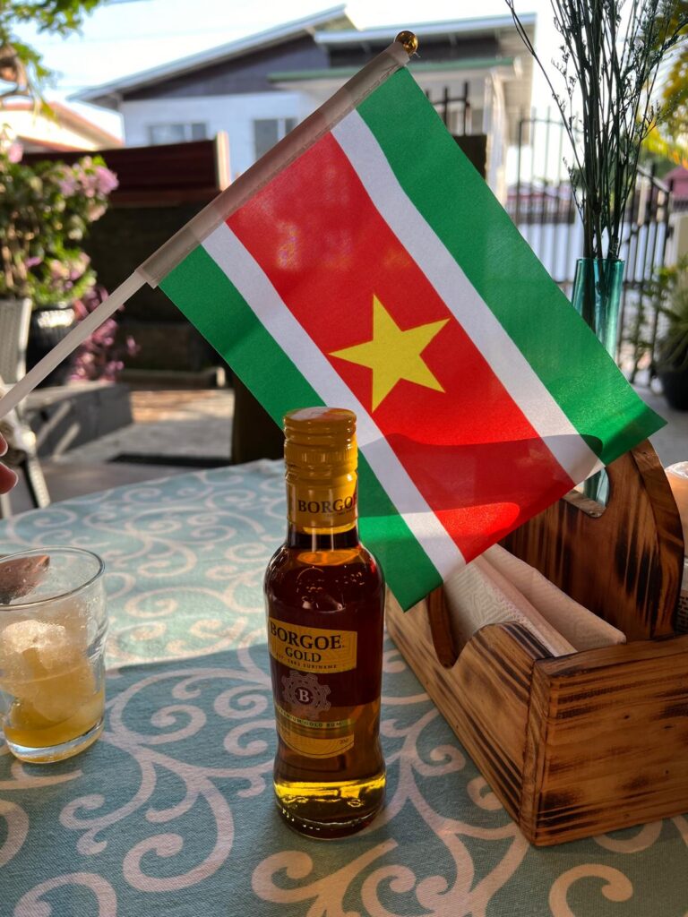 Een fles Borgoe Rum met daarachter de Surinaamse vlag