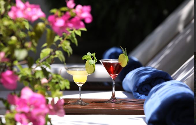 twee gegarneerde cocktails op een tafeltje naast comfortabele strandbedden