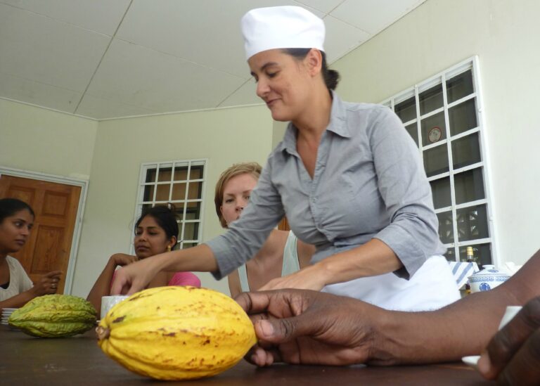 vrouw met koksmuts en gele cacao vrucht geeft cacao workshop aan reizigers
