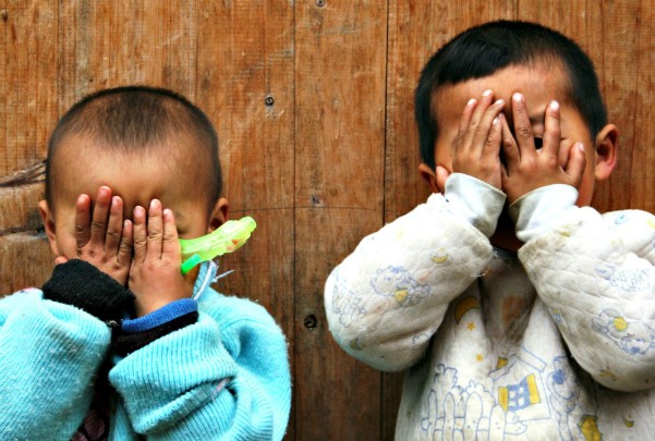 twee chinese jonegetjes spelen kiekeboe voor houten woning