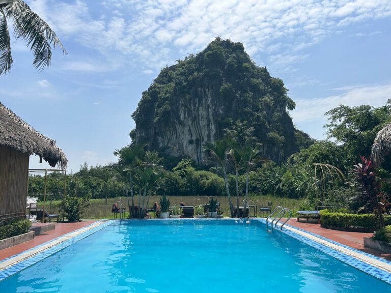 een groot zwembad in Tam Coc, vanuit het zwembad zie een grote rotsachtige berg in de verte.
