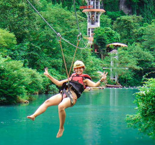 een vrouw glijdt met een zipline over het groenblauwe water tussen de bomen door