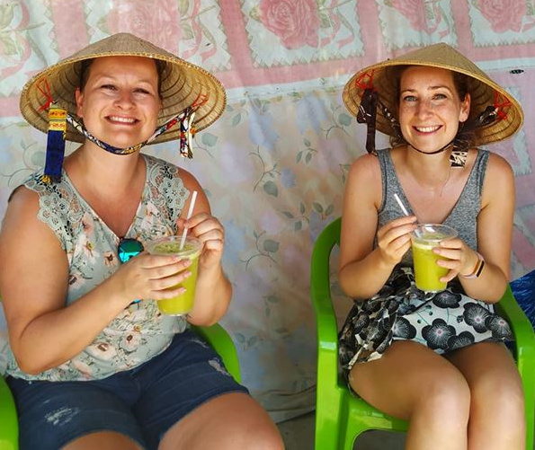 twee vrouwen met Vietnamese hoeden op drinken een sapje met een rietje