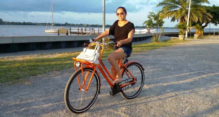 vrouw fiets op oranje fiets langs rivier in Paramaribo