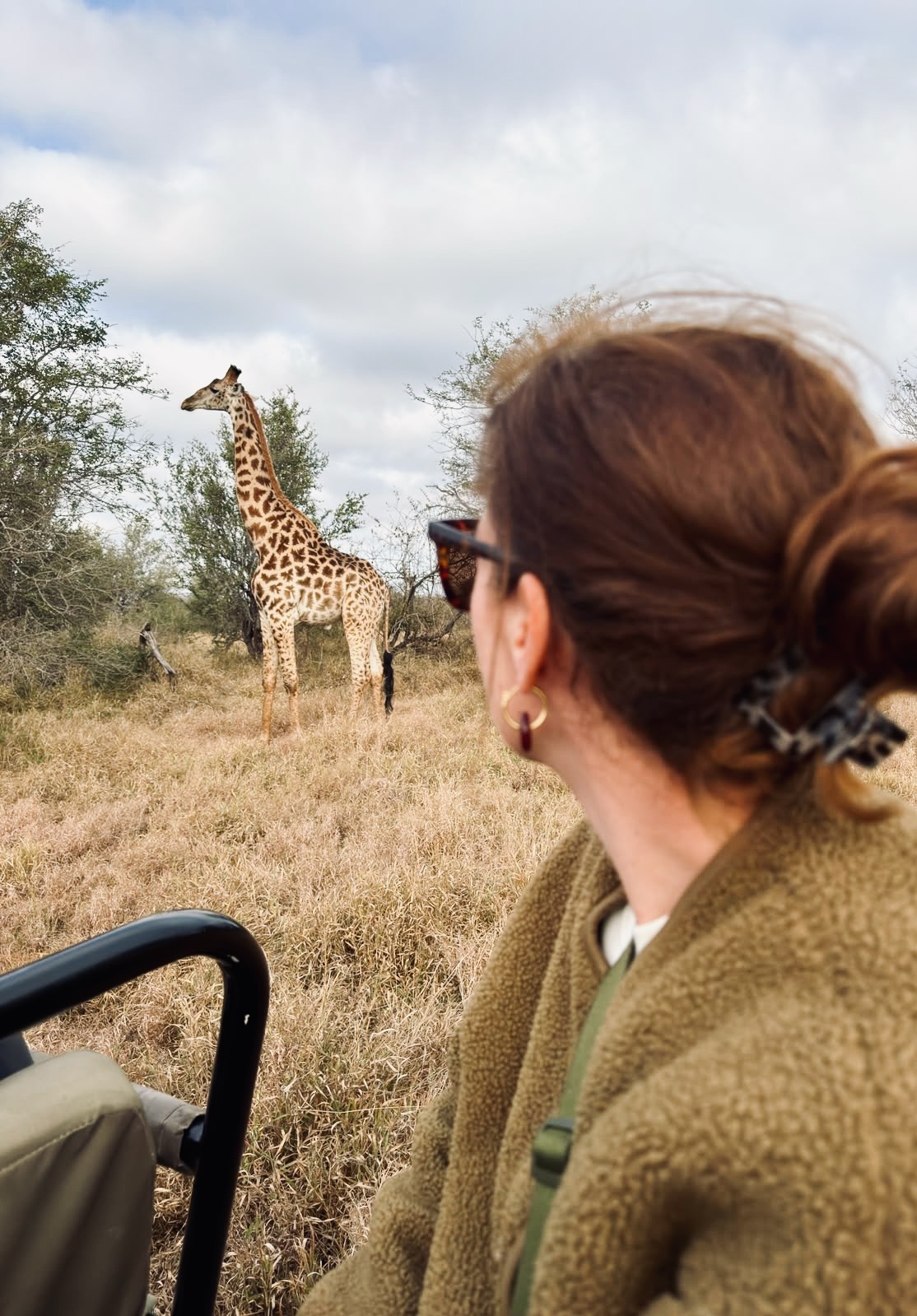 Vrouw die vanuit een safari jeep kijkt naar een voorbij lopende giraf in Zuid-Afrika