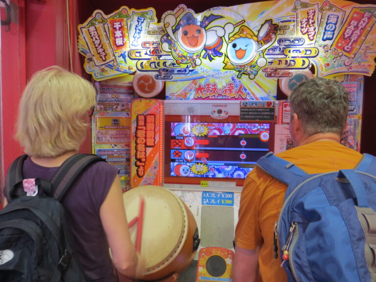reizigers spelen op een Taiko no Tatsujin arcadekast, een populaire Japanse ritmegame waarbij spelers op een virtuele trommel slaan