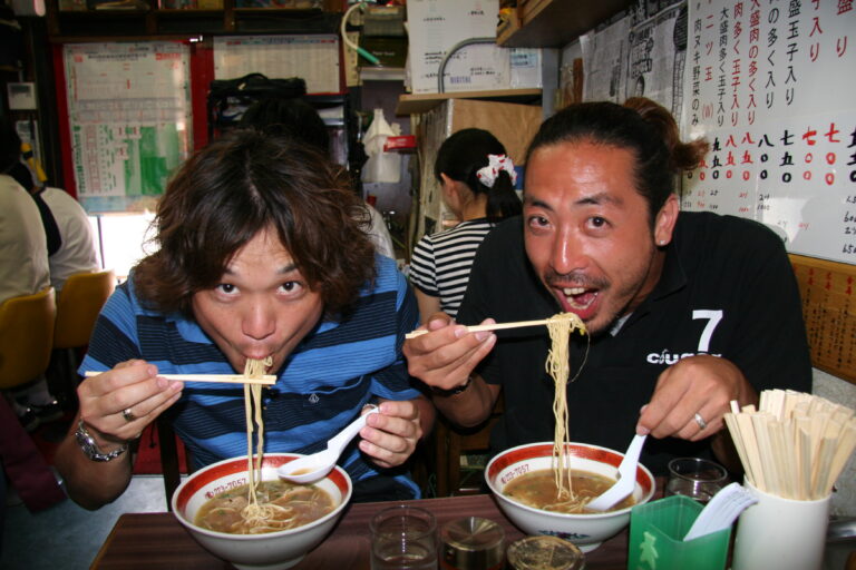 twee aziatische mannen slurpen van hun kom noedelsoep in Japan