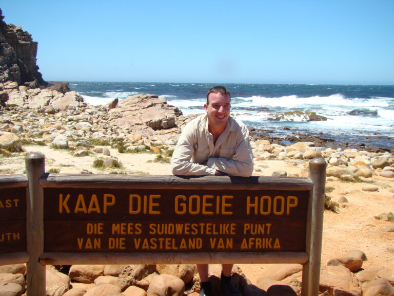 een man staat bij het 'kaap die goeie hoop' naambord