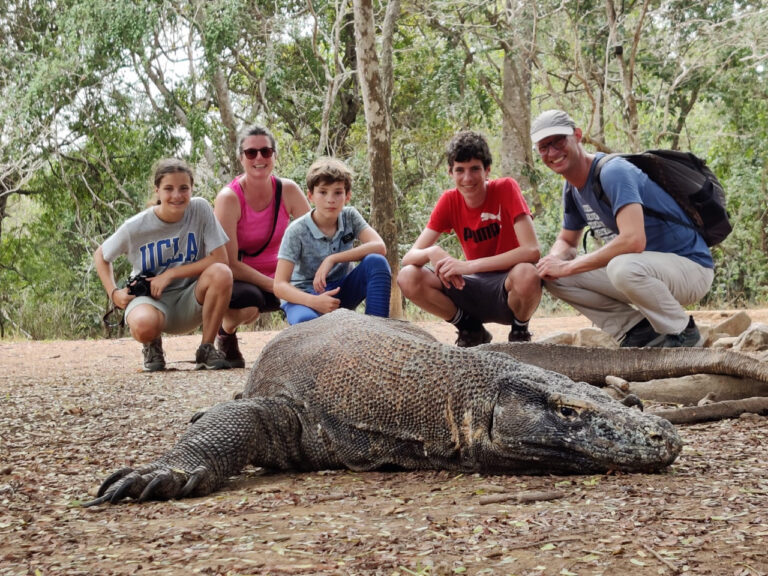 gezin van vijf zit gehurkt achter een metersgrote komodovaraan op de komodo eilanden in indonesie