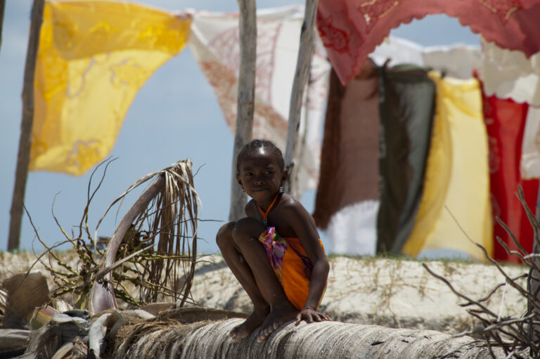 Lokaal meisje zittend op een boomstam met op de achtergrond was aan de waslijn in Madagaskar