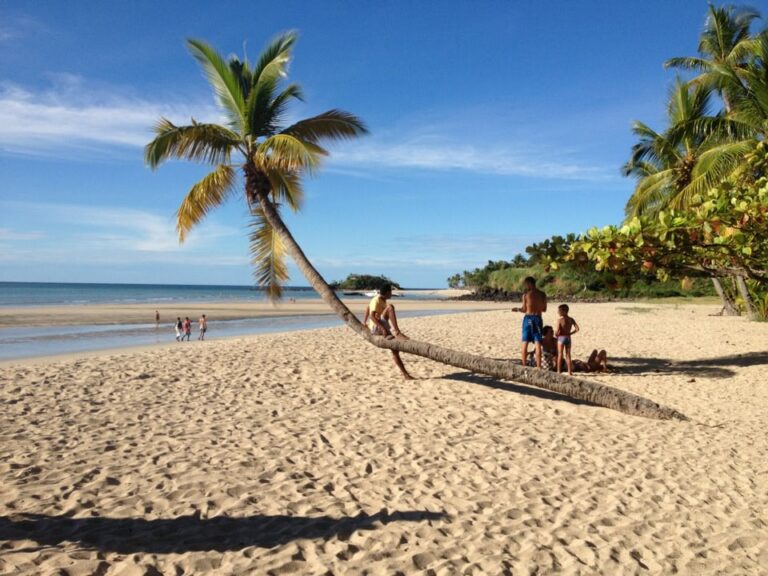 Strand bij Madagaskar met liggende palmboom en local zittend op de boomstam van de palmboom