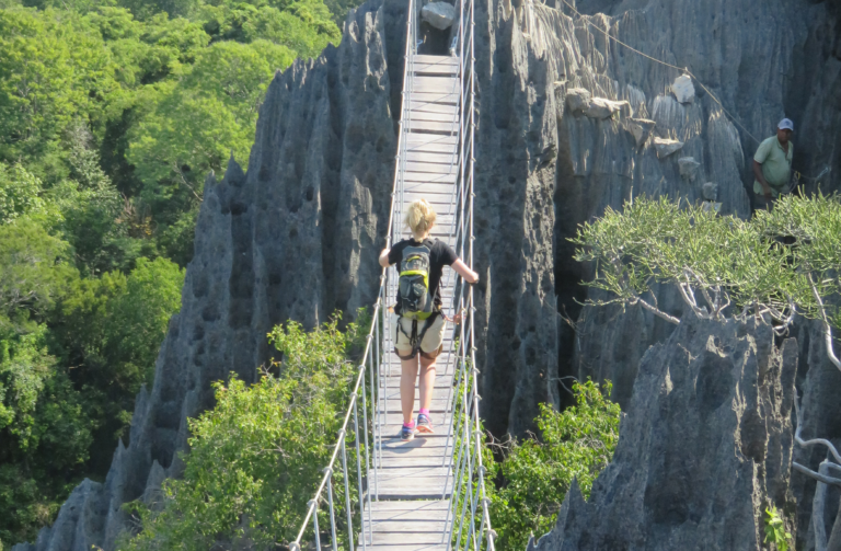 Vrouw met de rug naar de camera toe al wandelend op hangbrug tussen de rotsformaties in Madagaskar
