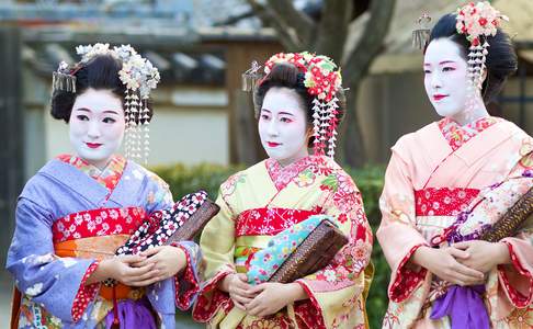 Vrouwen gekleed in traditionele Japanse Maiko-kleding, bestaande uit een rijk versierde rood-gouden kimono en uitgebreide witte make-up