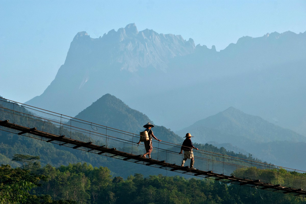 Hangbrug met twee locals erop uitkijkend op groene bergen in Maleisië
