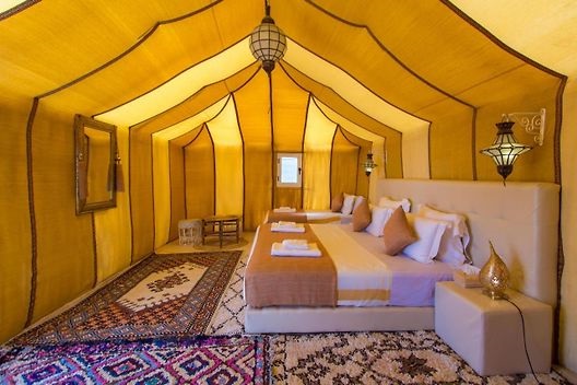 een sfeerfol ingerichte tent met een hoog plafond, groot bed en kleden over de grond