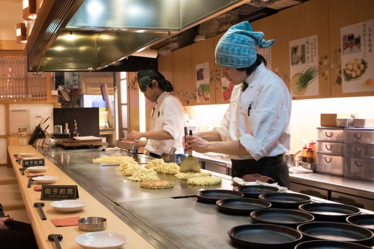 Japanse kok bereidt een hartige Japanse pannenkoek okonomiyaki op een teppanyaki-bakplaat