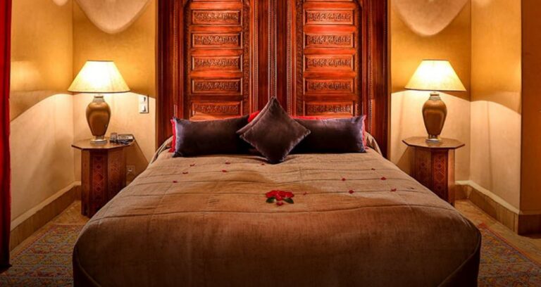 een groot comfortabel bed met donkere kussens in een sfeervol verlichte kamer