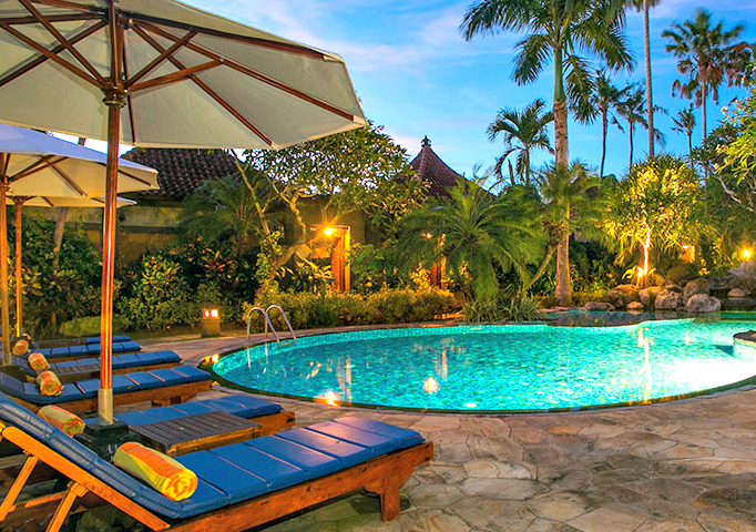 Zwembad van een resort omringd door palmbomen, ligbedjes en parasols